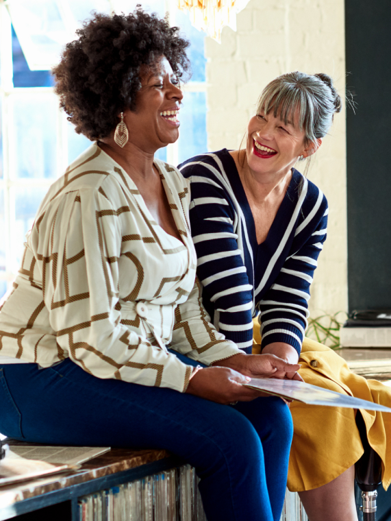 Two women sitting on a countertop top laughing together