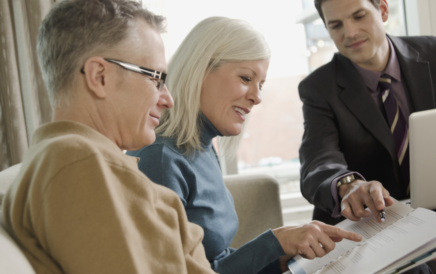 An older couple sitting on a couch looking over documents with a younger man going over the document with them